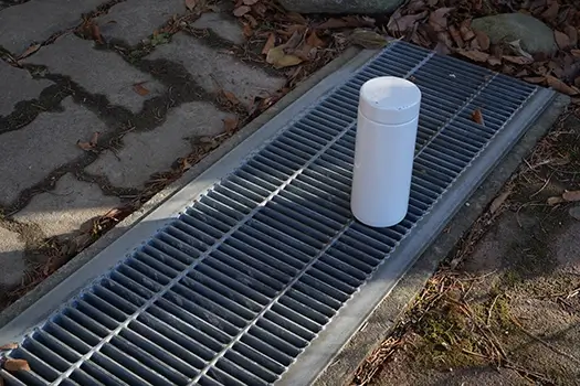 A white container sits on a grate in the ground. The container is empty and the grate is dirty